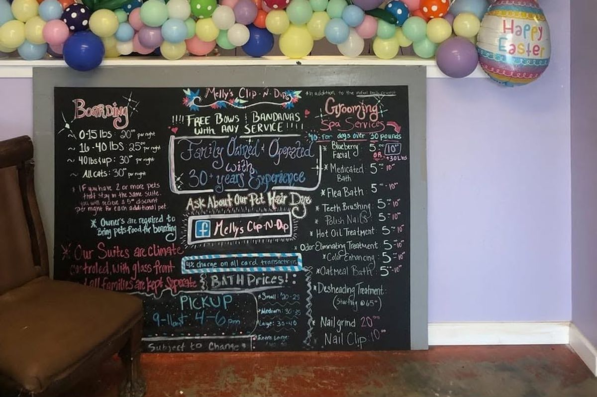 The shop's chalkboard price list with the boarding rates, bath prices and spa add-ons, under Easter balloons